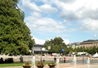 The statue Solsångaren surrounded by summer greenery in Strömparterren. View toward Kungsträdgården, and a glimpse of the Royal Opera in the background. Photo: Rhododendrites (CC BY-SA 4.0)
